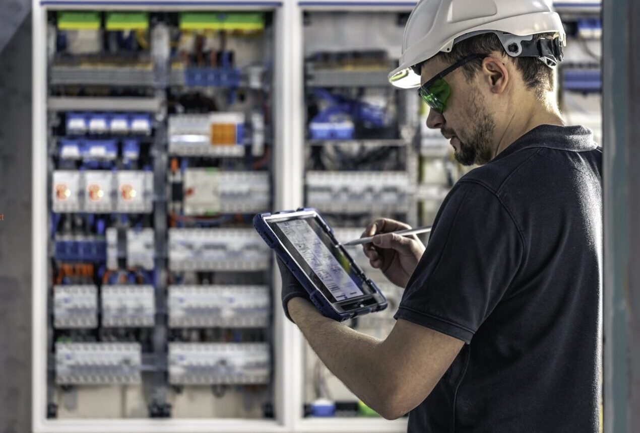 Man, an electrical technician working in a switchboard with fuses. Installation and connection of electrical equipment. Professional uses a tablet. Copy space.